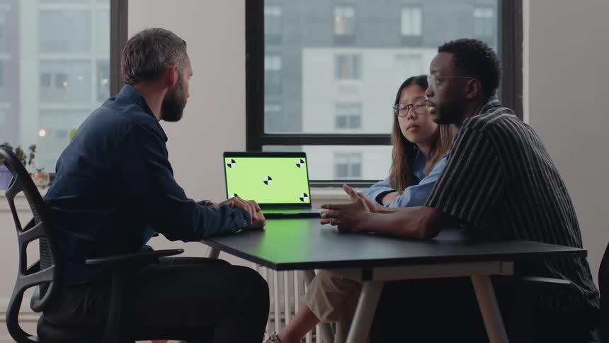 Three people having an office discussion regarding a laptop