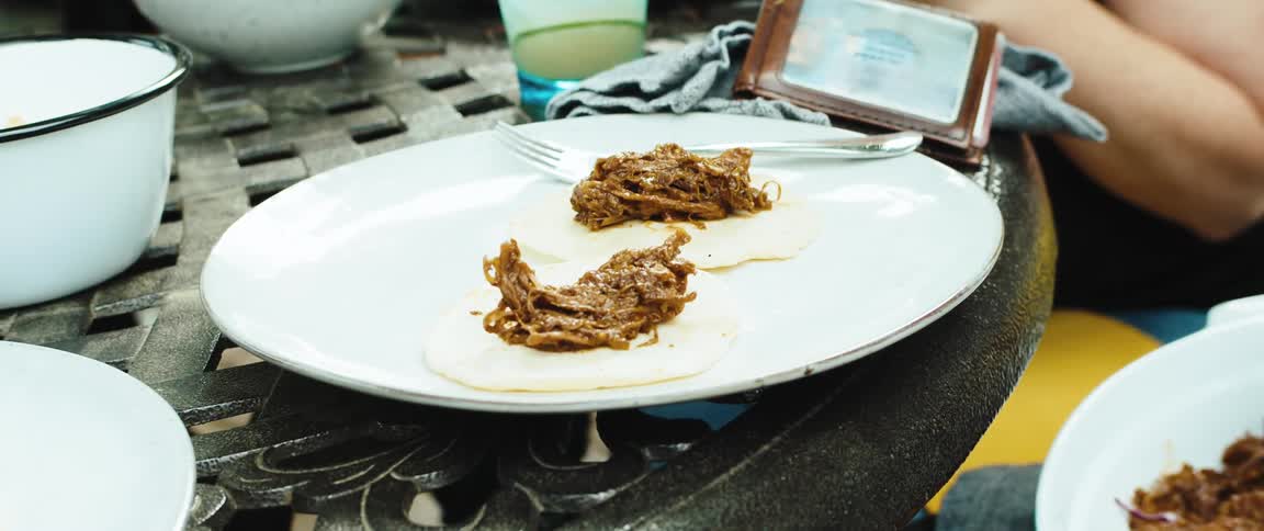 Closeup of hands serving saucy noodles onto a white plate outdoors