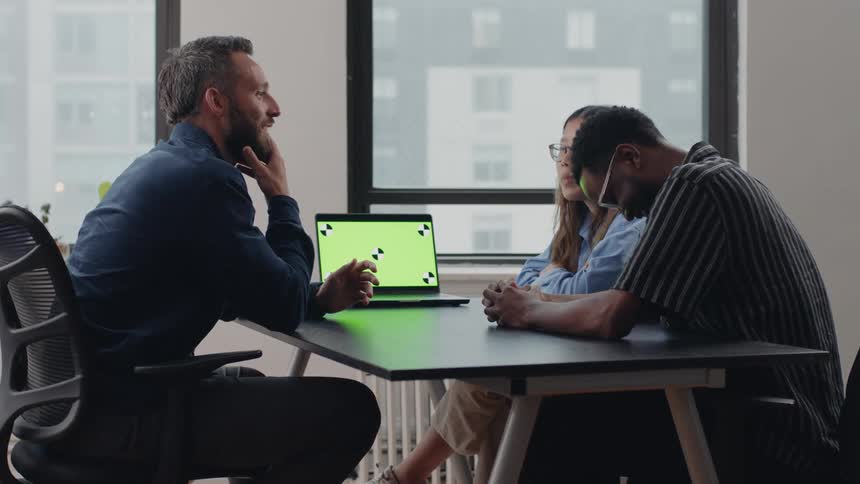 Three people having an office discussion around a laptop
