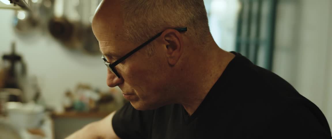 A man wearing glasses in a kitchen making a stirring motion with his arm