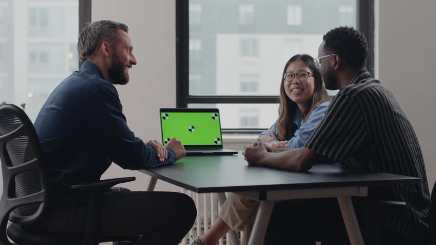 Three individuals seated around a table in the office with a laptop open on the table