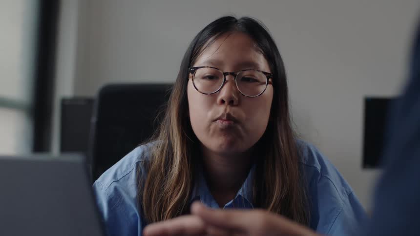 A young woman sitting in front of a laptop explaining or lecturing on a meeting in the office
