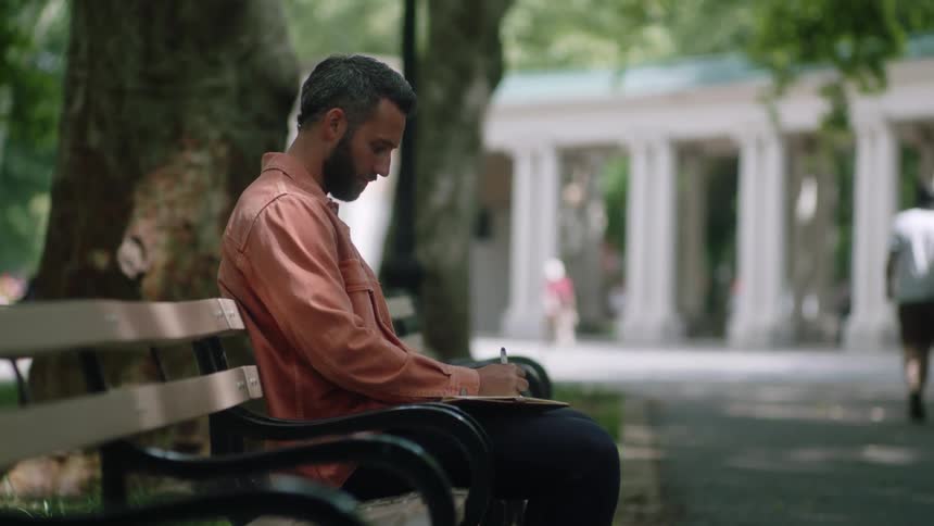 Man sitting on a park bench writing in a notebook