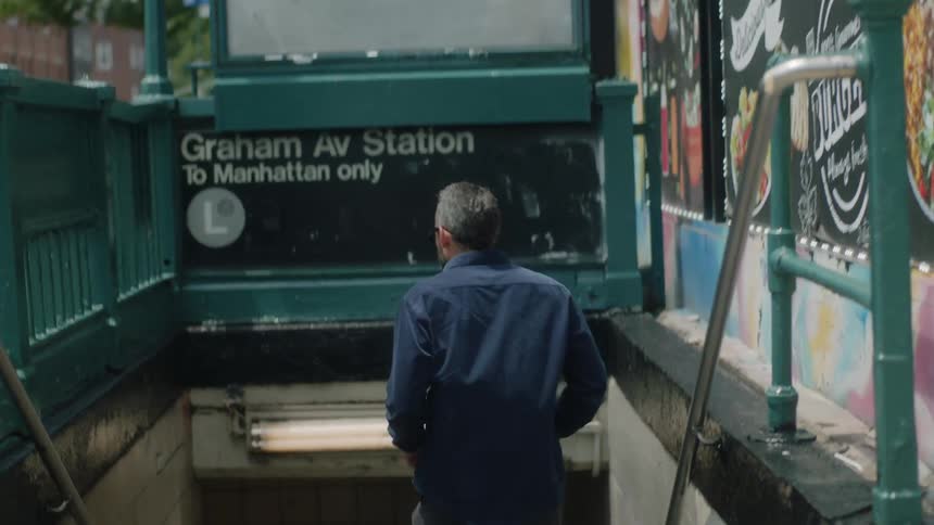 A man looks around and then goes down stairs into the subway system