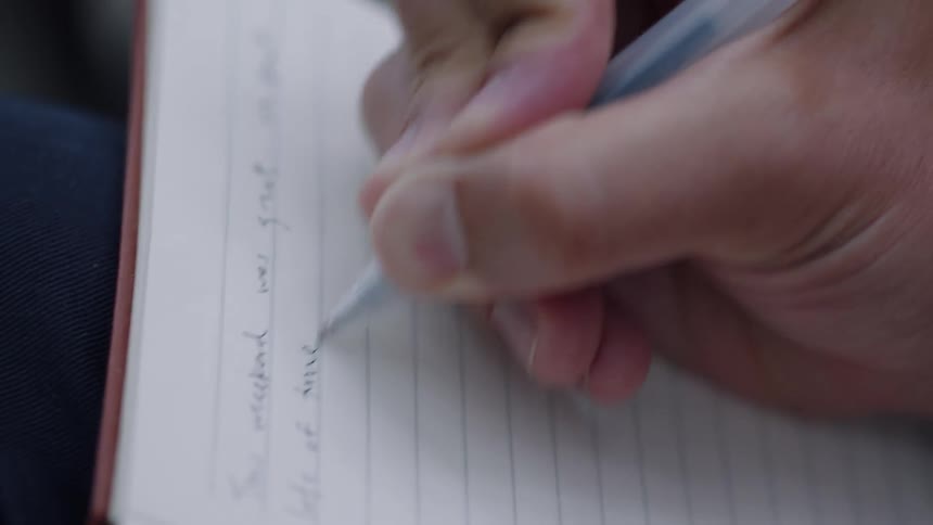 A closeup of a persons hand writing in cursive on a lined notebook with a pen