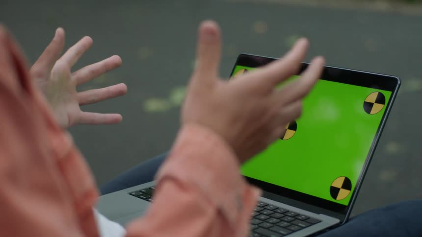 Man gestures during a video call on a laptop while pedestrians walk past