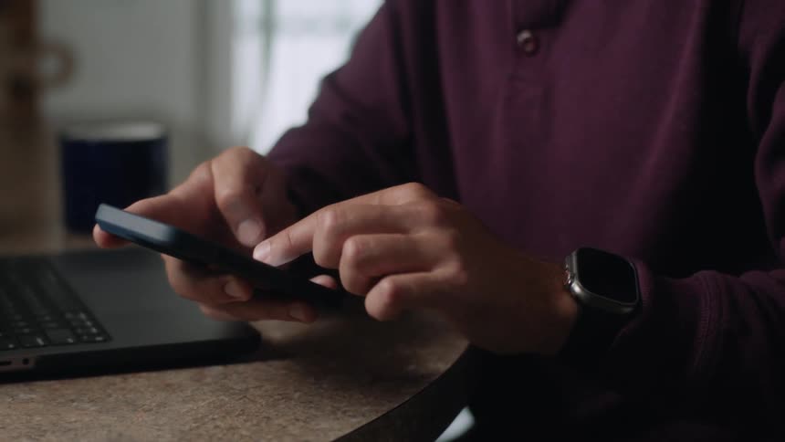 Pair of hands typing on a laptop and then using the cell phone