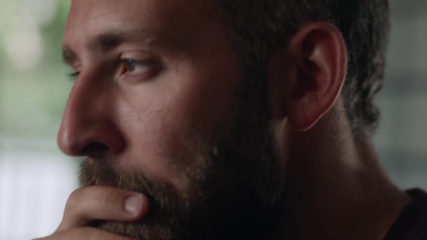 Close up of the face of a bearded man drinking a cup of coffee at home