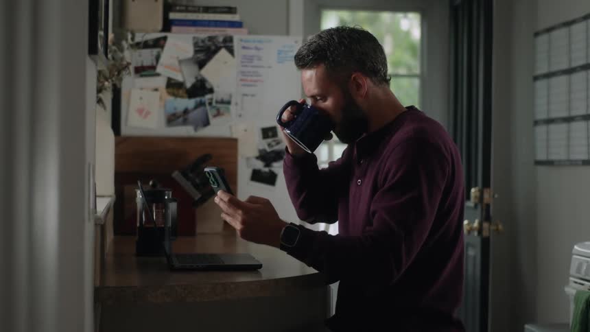 A man is sitting at a counter at home while typing on a laptop pc