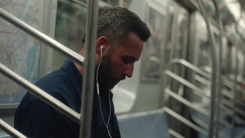 A man wearing earbuds while riding the subway stands up to exit the train