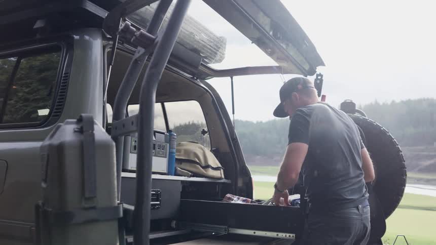 A construction worker roots around in a tool drawer in his vehicle as it rains