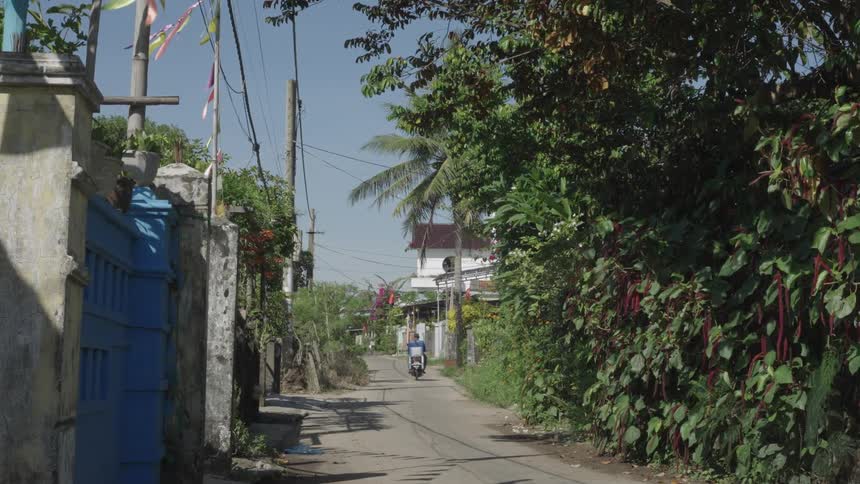 Man riding a motorcycle in a narrow alley in a city surrounded by greenery