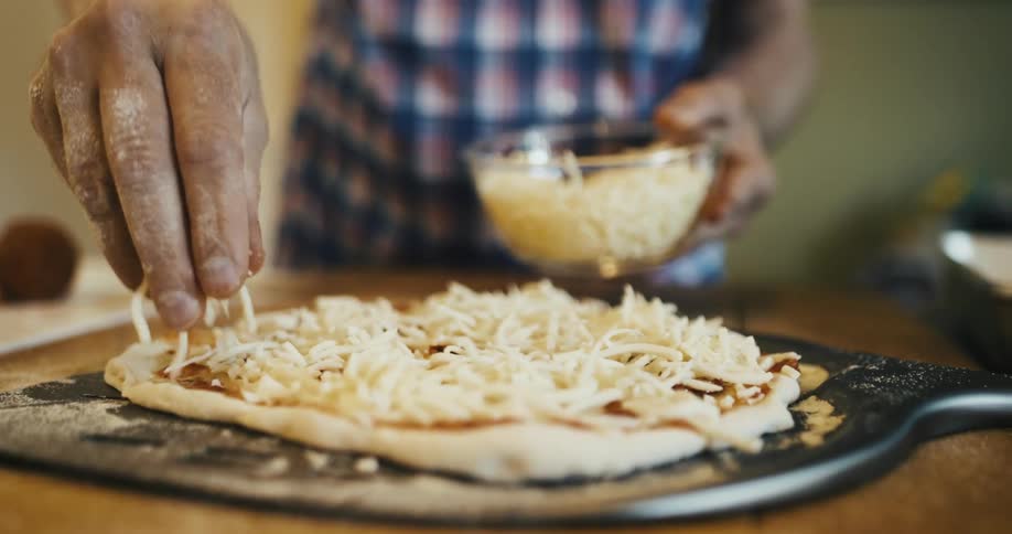 Closeup on pair of hands pouring grated cheese onto pizza dough