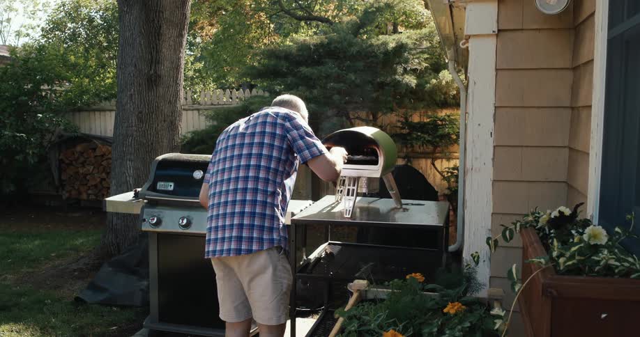 A dad placing a pizza into an oven in his backyard