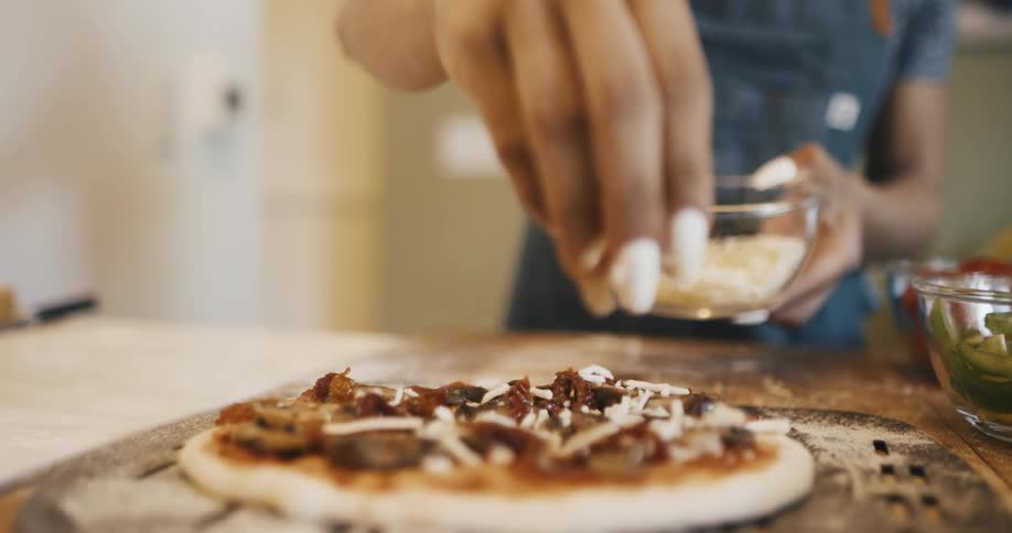 Closeup of a womans hand pouring grated cheese on top of a pizza