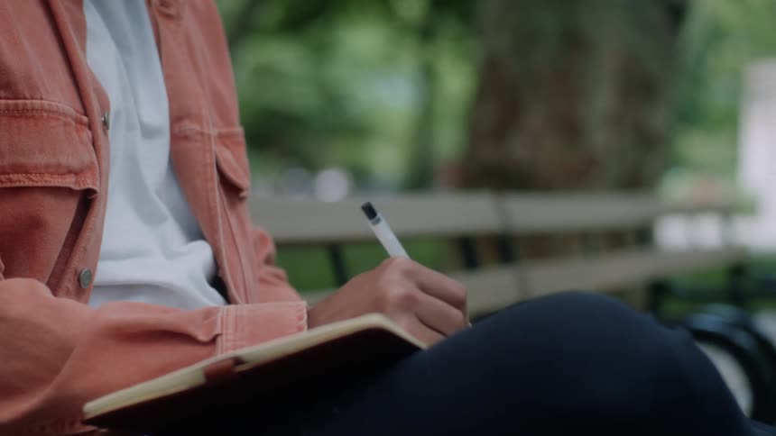 Man sitting on a park bench writing in a book