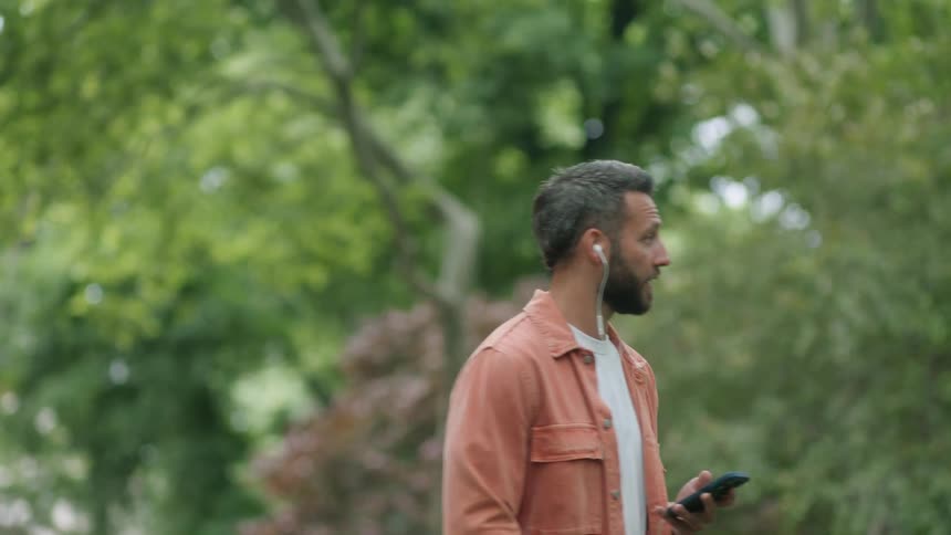 A man walks outdoors while using a headset to talk on his smartphone