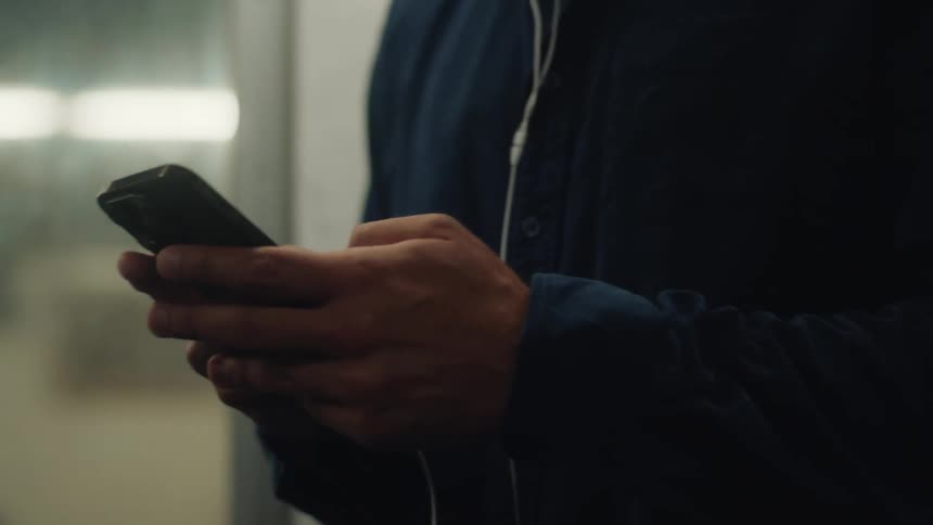 Close up of the hands and face of a man texting on a phone while riding the subway