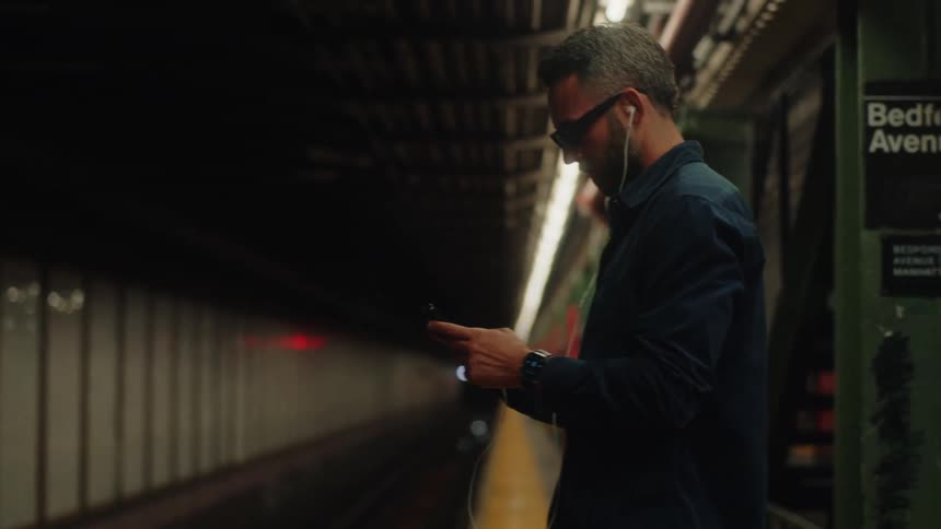Man using his cell phone while waiting for the train to arrive at a station