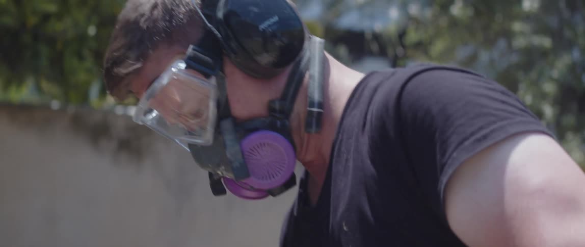 Man in protective gear working with a jackhammer in a backyard