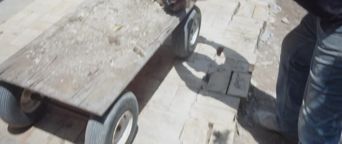A worker piling up bricks over a small trolley in the backyard on a sunny day