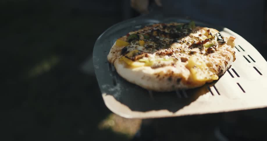 A person carries a cooked pizza on a large spatula