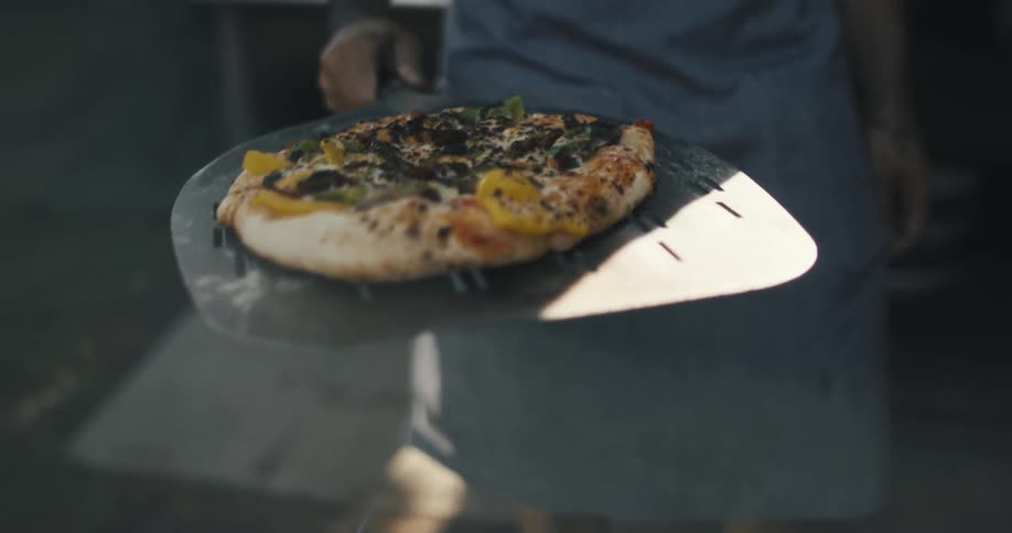 Small baked pizza being carried to a pizza oven
