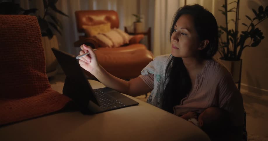 Mother holds baby while considering contents on computer screen