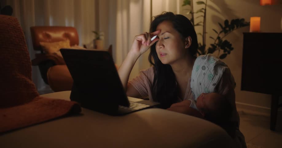 A tired woman drawing on a touchscreen laptop while sitting on the floor of a dimly lit living room