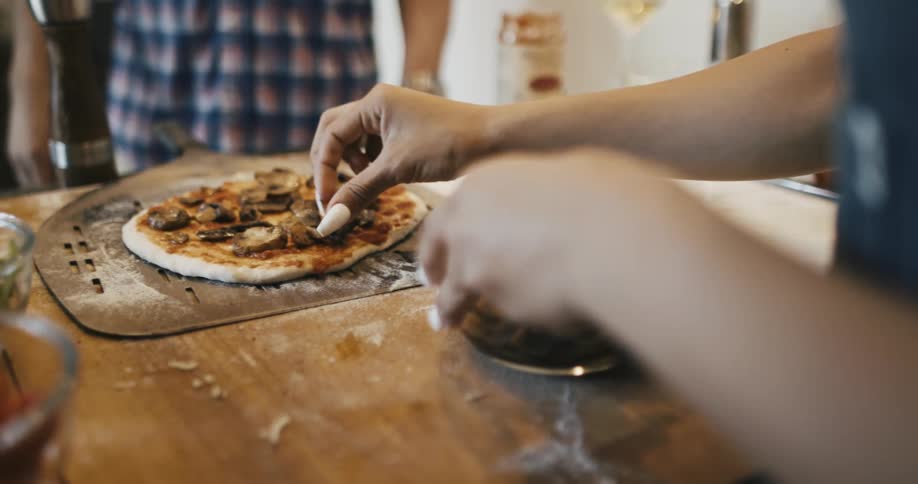 Pair of hands seasoning a pizza dough