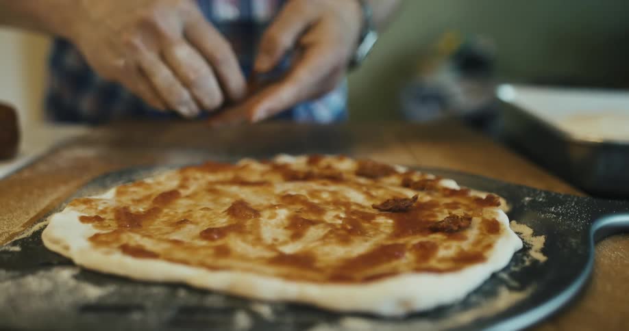 A closeup view of hands spreading sauce on a pizza base placed on a pan
