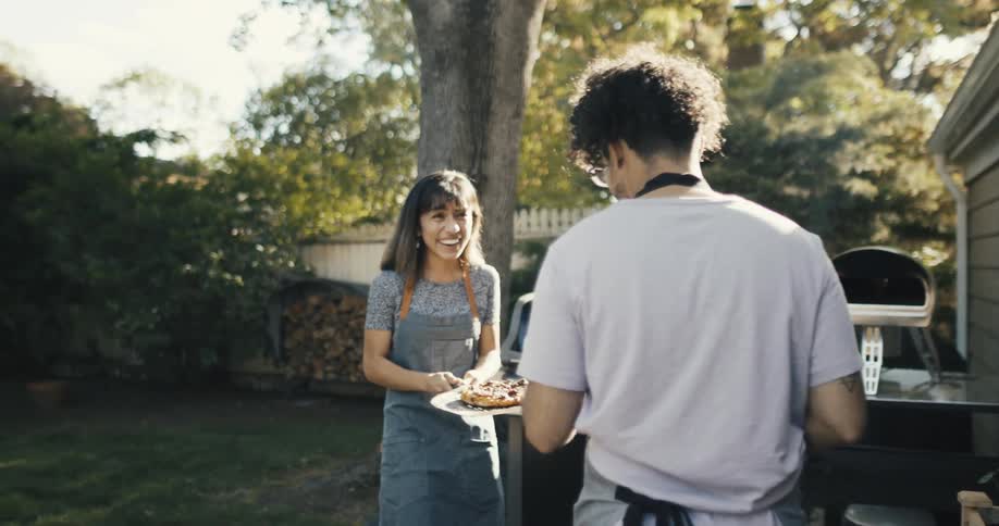 Man filming a woman holding a freshly baked pizza with a spatula