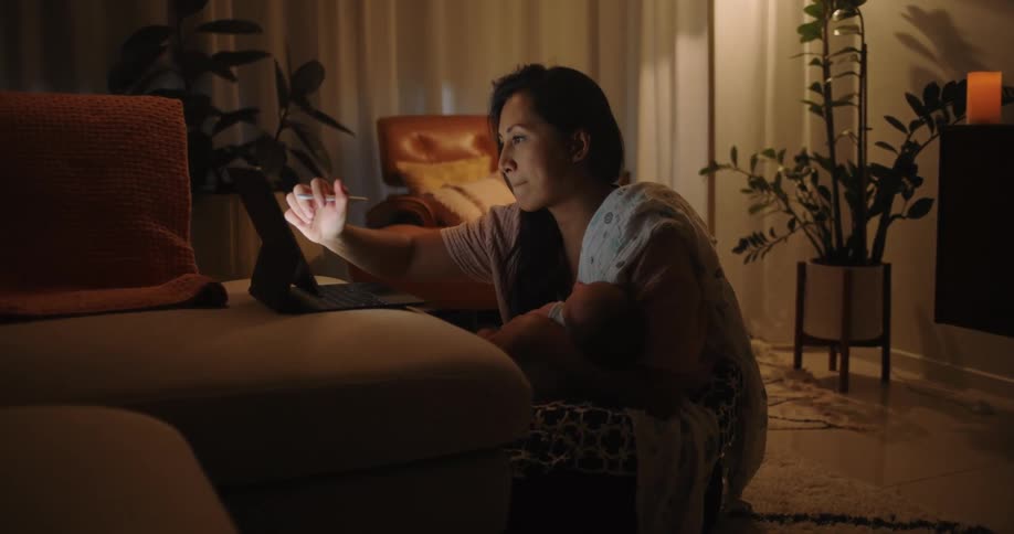A woman sitting on the floor of the living room at night drawing on a laptop with a touchscreen