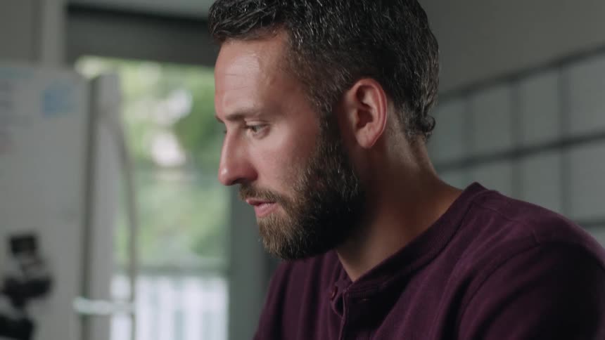Close up of the face of a bearded young man laughing while working from home