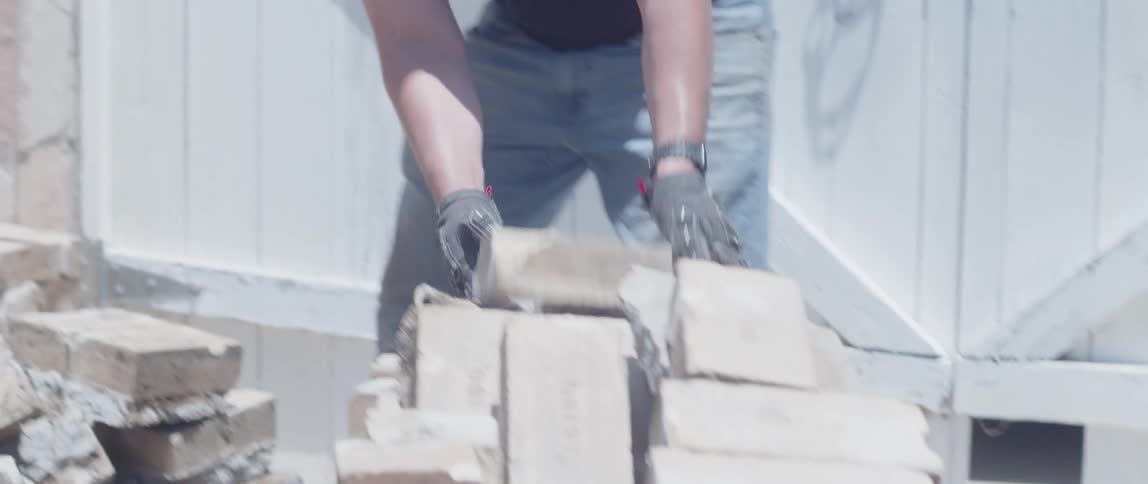 Man with gloves picking up concrete blocks and throwing them on top of another pile