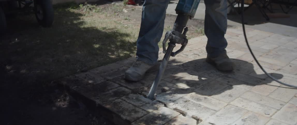 A worker in heavyduty boots operates a jackhammer breaking up concrete
