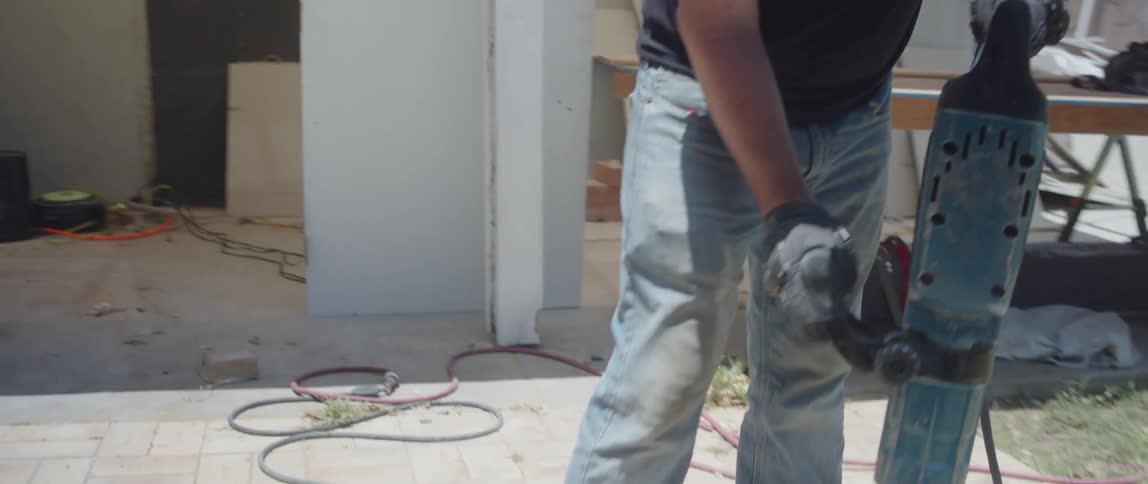 Man with protective mask working with a jackhammer on a floor in a backyard
