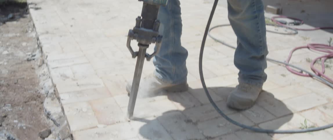 Man with a mask and concentrated using a jackhammer to cut the concrete floor
