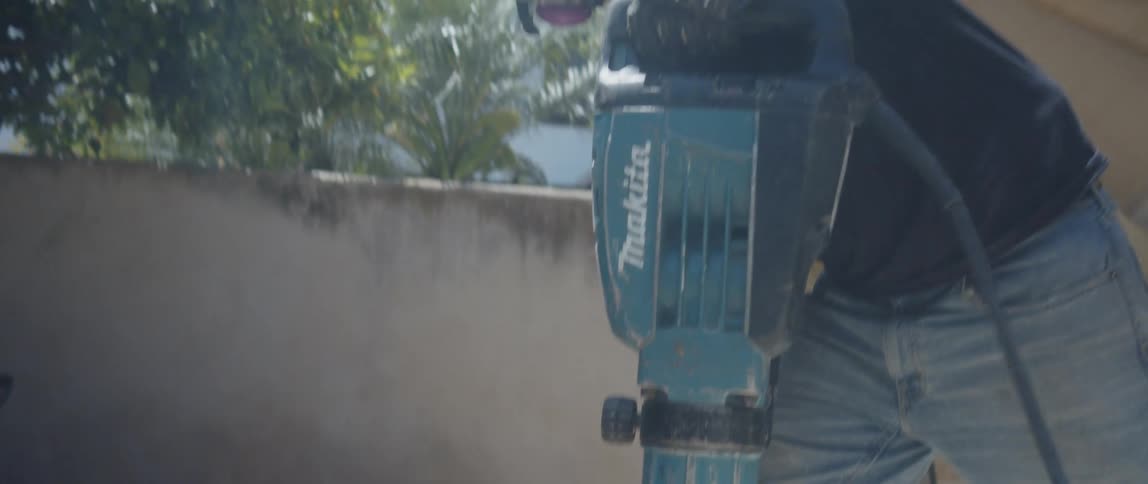 A worker in heavyduty boots operates a jackhammer breaking up concrete