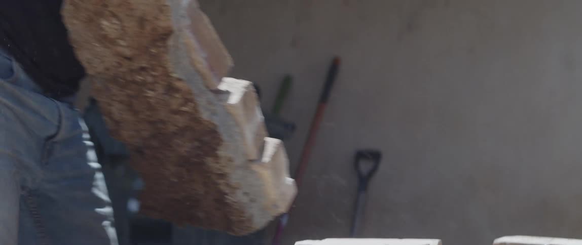 Pair of gloved hands of a man picking up a concrete block and placing it on top of other stones