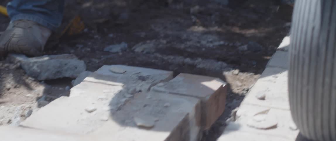 A worker picking up bricks from the ground and placing them over a small cart