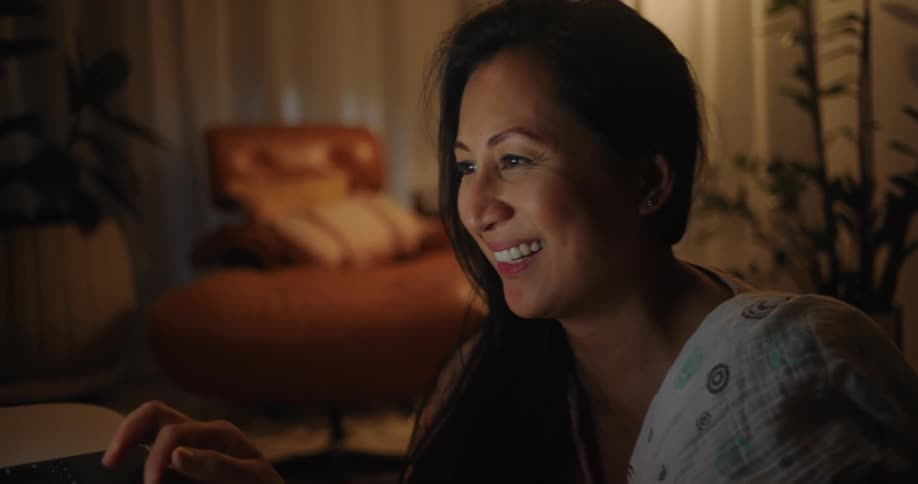 An asian woman using a laptop starts smiling and laughing