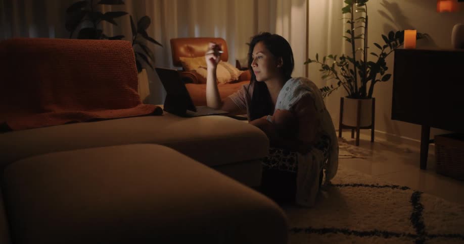 A woman rights on a laptop screen in a living room while seemingly stressed