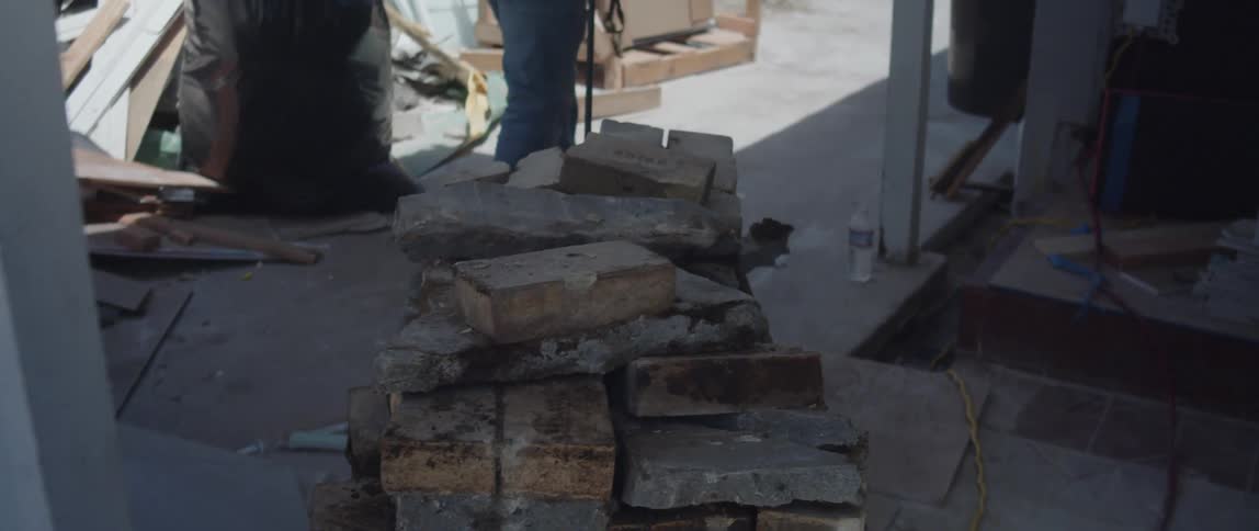 A man drags a cart of bricks though the yard