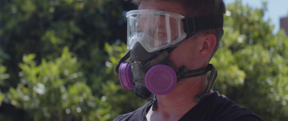 A man wearing a dual filter respirator mask and work gloves on a sunny day in the backyard