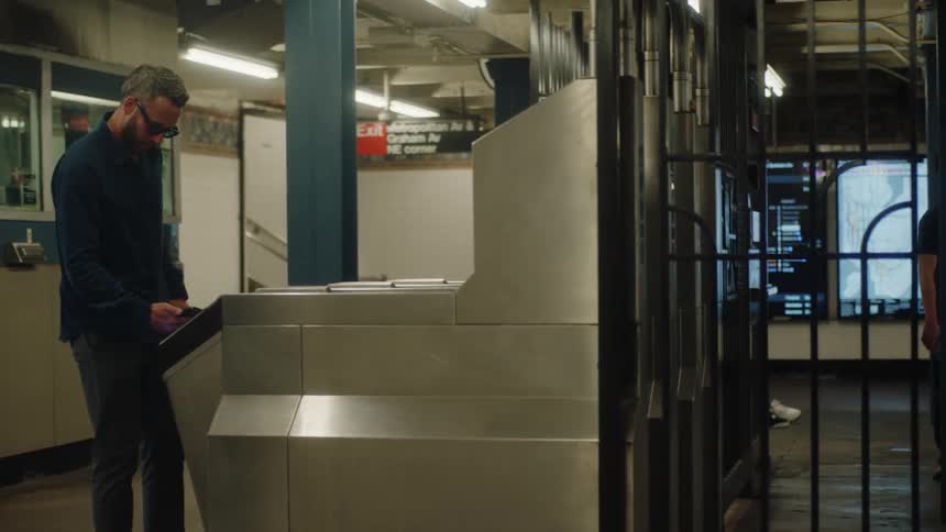 A man passes through a turnstile in a subway station paying the fare with a smartphone