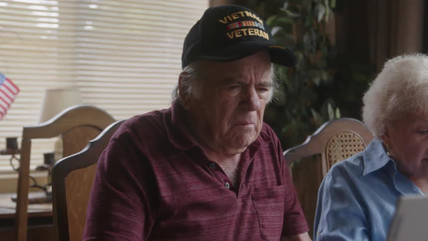 Elderly man and woman sitting talking and using a laptop together at the table