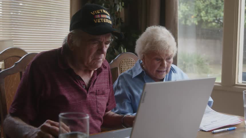 Elderly couple sitting together at a table looking at documents and a laptop