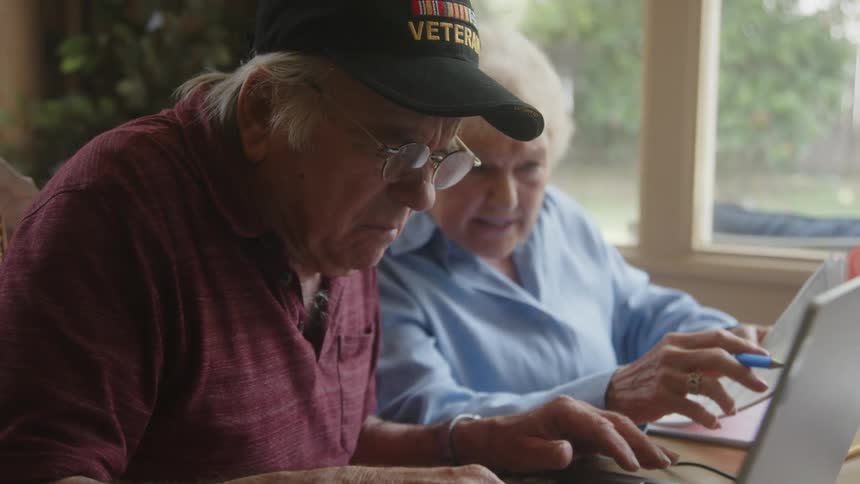A man and woman look at paperwork and use a laptop