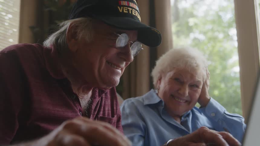 A man and woman laugh while looking at a laptop